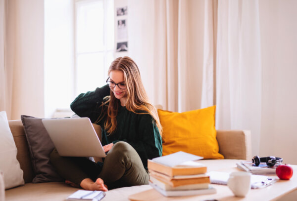 A young woman with a laptop, sitting on the couch in her apartment.